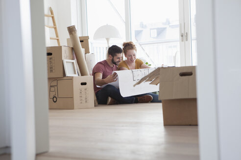 Young couple in new flat with cardboard boxes holding ground plan - RBF002861