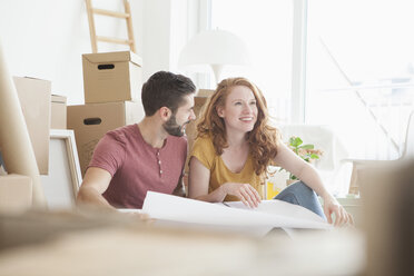 Young couple in new flat with cardboard boxes holding ground plan - RBF002779