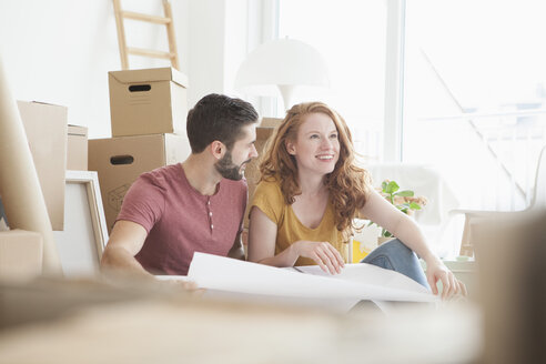 Junges Paar in neuer Wohnung mit Pappkartons, die den Grundriss halten - RBF002779