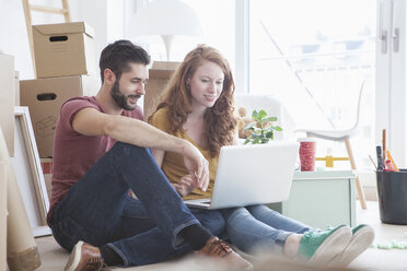 Young couple in new flat with cardboard boxes, using laptop - RBF002781