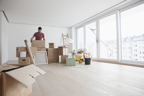 Junger Mann in neuer Wohnung packt Kartons aus, lizenzfreies Stockfoto