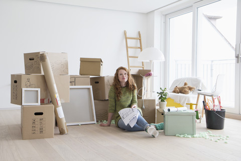 Junge Frau in neuer Wohnung mit Pappkartons und Grundriss, lizenzfreies Stockfoto