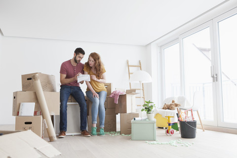 Junges Paar in neuer Wohnung mit Pappkartons und Blick auf den Grundriss, lizenzfreies Stockfoto