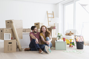 Young couple in new flat with cardboard boxes, sitting on floor - RBF002867