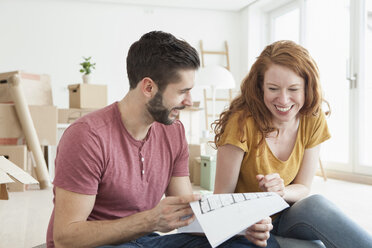 Young couple in new flat with cardboard boxes looking at ground plan - RBF002869