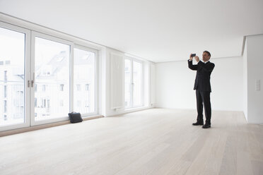 Estate agent standing in empty apartement, taking pictures - RBF002798