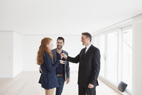 Immobilienmakler bei der Schlüsselübergabe an ein junges Paar - RBF002806