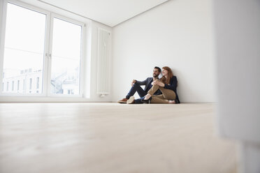 Junges Paar sitzt auf dem Boden ihrer neuen Wohnung - RBF002813