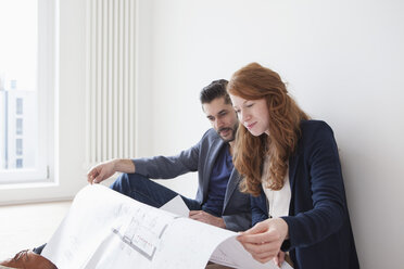 Young couple sitting on floor of their new flat, looking at ground plan - RBF002815