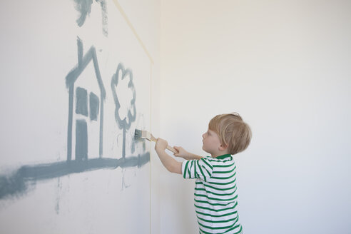 Little boy painting house and tree on wall of his new room - RBF002826