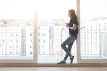 Young woman leaning at sliding door of balcony looking at distance - RBF002753