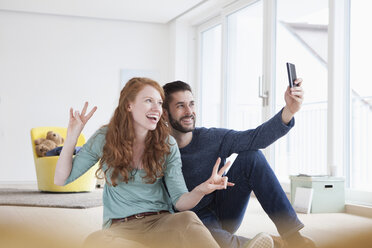 Lächelndes junges Paar macht ein Selfie mit Smartphone im Wohnzimmer - RBF002765