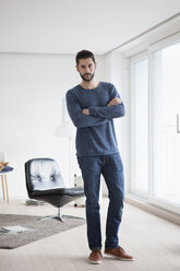 Portrait of young man with crossed arms standing in his living room - RBF002840