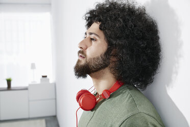 Young man with red headphones leaning against wall at home - PDF001078