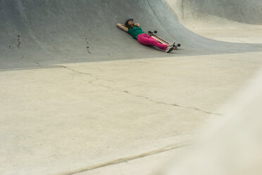 Young woman lying besides her skateboard having a rest - UUF004607