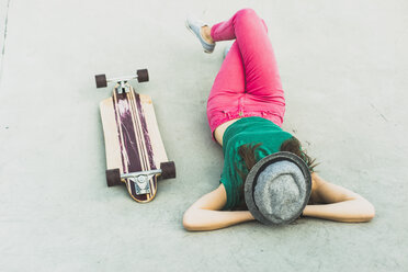 Young woman lying besides her skateboard having a rest - UUF004610