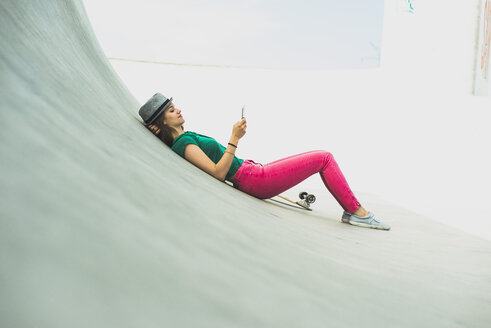 Junge Frau auf dem Skateboard, die sich ausruht und auf ihr Smartphone schaut - UUF004611