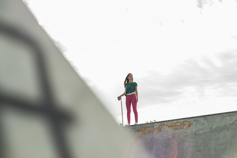 Junge Skateboarderin steht auf einer Mauer und schaut in die Ferne, lizenzfreies Stockfoto