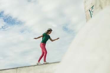 Junge Frau balanciert auf einer Mauer in einem Skatepark - UUF004620