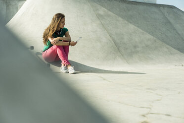 Young skate boarder sitting in a skatepark using smartphone - UUF004627