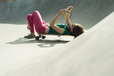 Junge Frau liegt auf ihrem Skateboard und benutzt ihr Smartphone - UUF004628