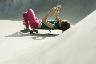 Young woman lying on her skateboard using smartphone - UUF004628