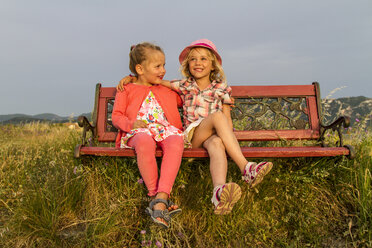 Greece, Corfu, Afionas, two little girls sitting side by side on a bench at evening twilight - JFEF000683