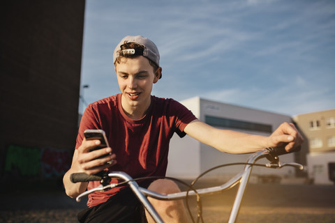 Junger Mann mit BMX-Fahrrad schaut auf sein Handy, lizenzfreies Stockfoto