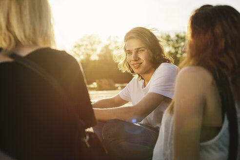 Freunde sitzen bei Sonnenuntergang im Freien zusammen - GCF000093