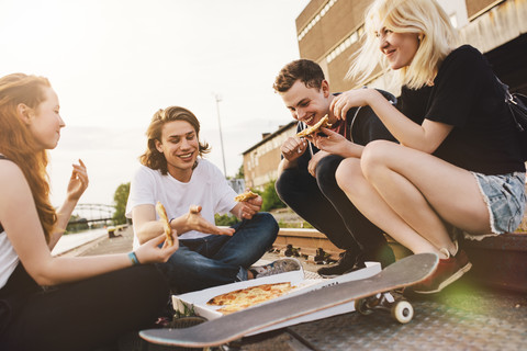 Freunde sitzen im Freien zusammen und teilen sich eine Pizza, lizenzfreies Stockfoto