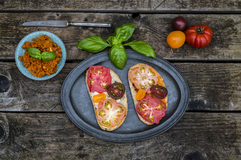 Tomatenbrot mit Heirloom-Tomaten und Basilikum auf einem Holztisch - SARF001843