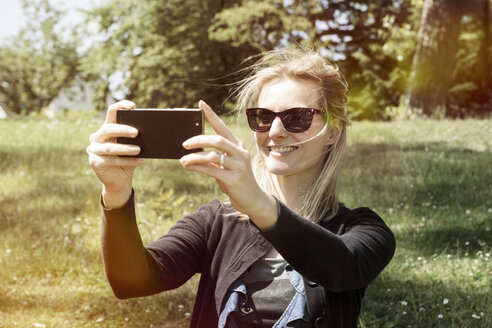 Lächelnde Frau mit Sonnenbrille macht ein Selfie mit ihrem Smartphone - CHPF000148