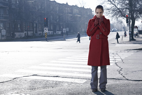 Frau in rotem Mantel steht an einer Kreuzung in einer grauen Stadt - MHCF000015