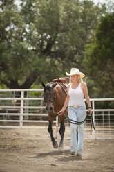Cowgirl leading horse out of a corral - ABAF001800