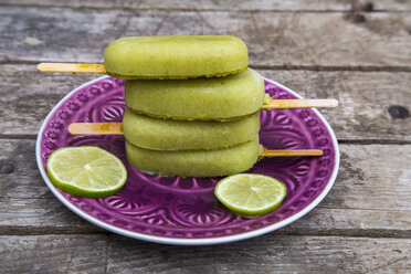 Stack of avocado ice lollies and slices of lime on plate - SARF001868
