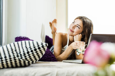 Relaxed young woman lying in bed with laptop looking up - UUF004739
