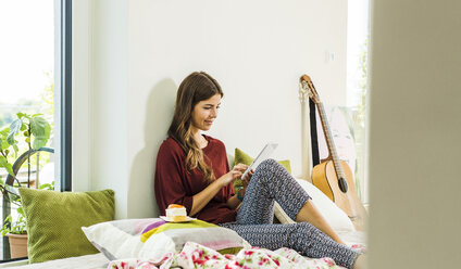 Entspannte junge Frau, die zu Hause im Bett ein digitales Tablet benutzt - UUF004679