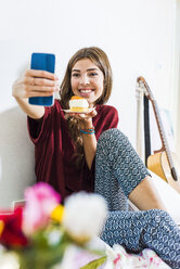 Entspannte junge Frau zu Hause im Bett nehmen selfie mit Stück Kuchen - UUF004680