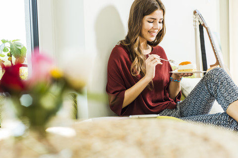 Entspannte junge Frau zu Hause im Bett und isst ein Stück Kuchen, lizenzfreies Stockfoto