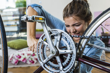 Gestresste junge Frau, die zu Hause ihr Fahrrad repariert - UUF004696