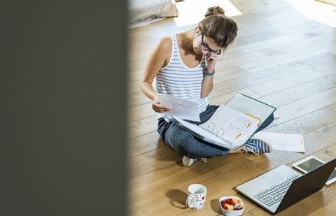 Junge Frau sitzt auf Holzboden mit Aktenordner und Laptop, lizenzfreies Stockfoto