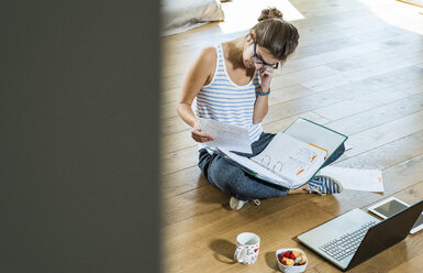 Young woman sitting on wooden floor with file folder and laptop - UUF004747