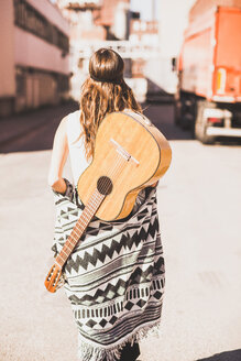 Young woman with guitar on her back walking on street - UUF004712