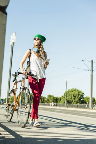 Junge Frau mit Fahrrad auf dem Bürgersteig mit Handy in der Hand, lizenzfreies Stockfoto