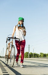 Young woman with bicycle on pavement looking at cell phone - UUF004727