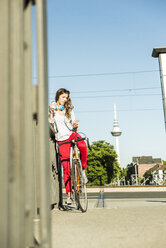 Young woman with bicycle on pavement looking at cell phone - UUF004731