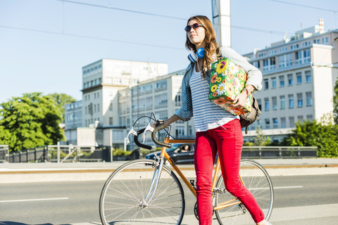 Junge Frau mit Fahrrad auf dem Bürgersteig mit Geschenkbox, lizenzfreies Stockfoto