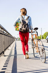 Young woman with bicycle on pavement holding gift box - UUF004736