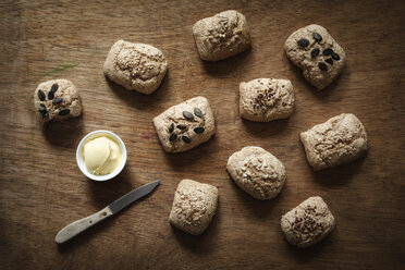 Verschiedene selbstgebackene Dinkelvollkornbrötchen, Butter und Messer auf Holz - EVGF001884