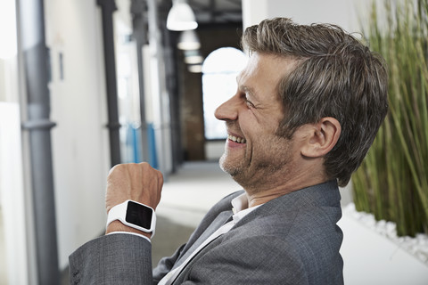 Lächelnder Geschäftsmann im Büro mit Smartwatch, lizenzfreies Stockfoto